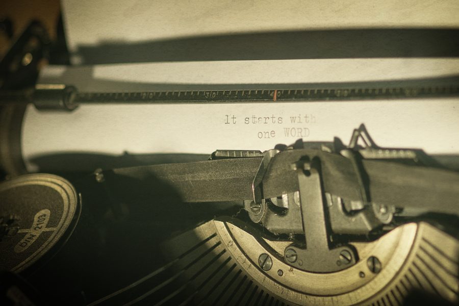 A vintage typewriter with the text "it starts with one WORD" written on a shee