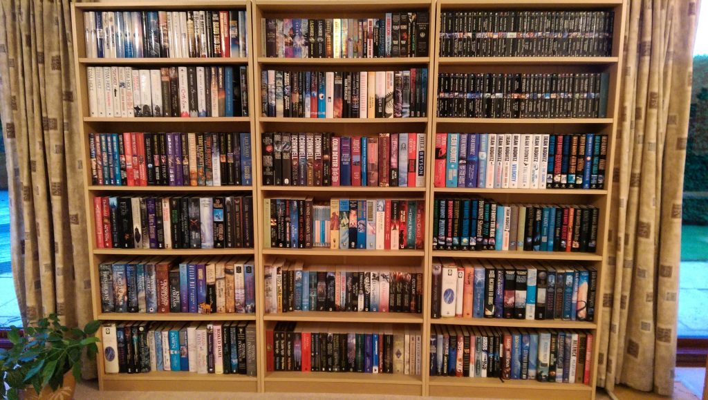 Photo of three large bookshelves filled with (mostly) hardback books. If you look closely, there is a full set of Gollanc Masterworks on the rightmost top two shelves, but that's not important right now.