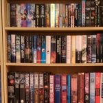 Closeup of bookshelves showing a number of hardbak and trade paperback books of various genres.